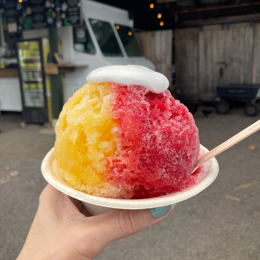 Stacy's hand holding cup of shave ice topped with coconut cream