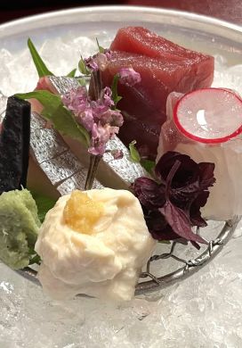 Small plate of sashimi garnished with flowers and resting on a bed of ice