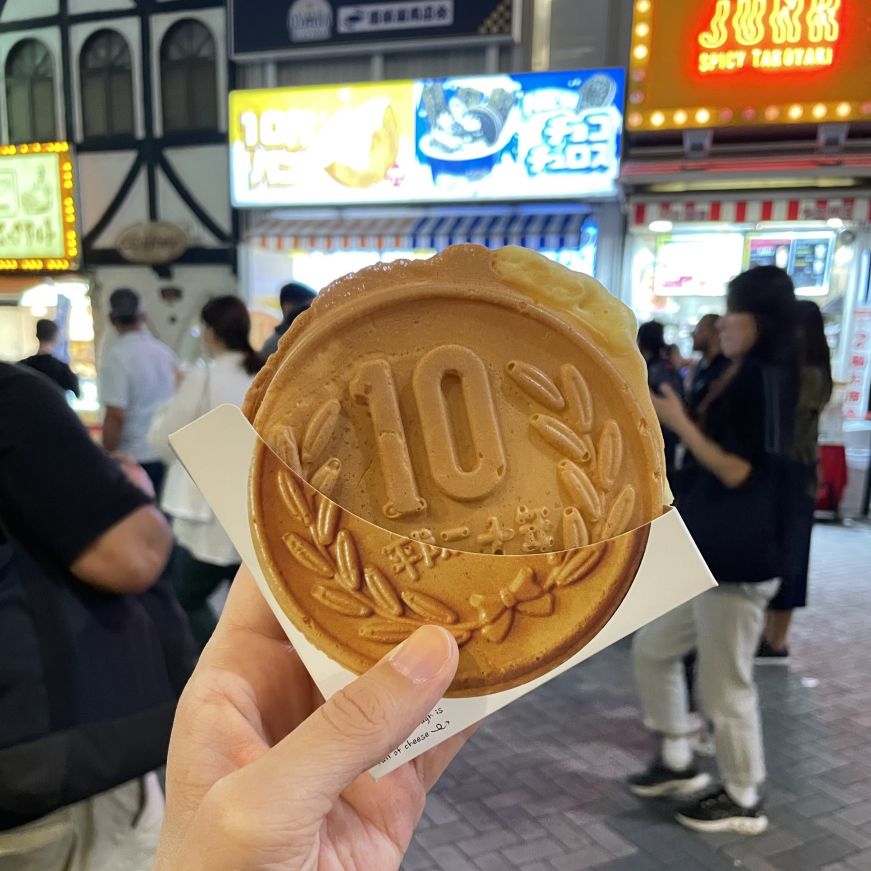 Stacy's hand holding a piece of crispy bread shaped like a 10 yen coin