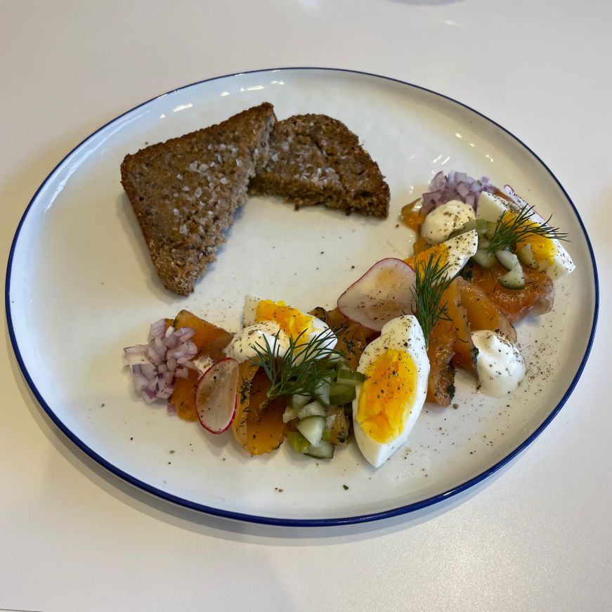 Plate with two pieces of rye bread and an artistically arranged spread of hard boiled eggs, smoked salmon, and fresh dill