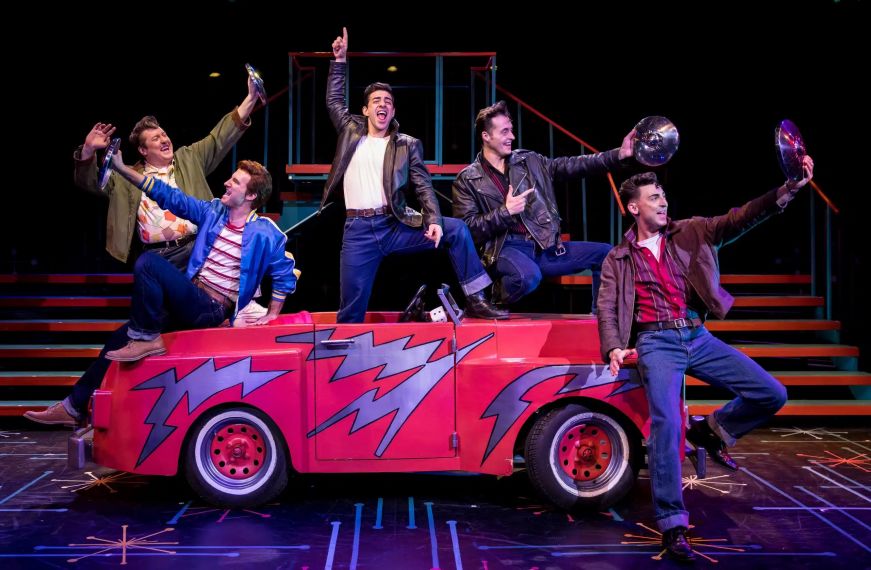 Actors on stage singing around a prop car