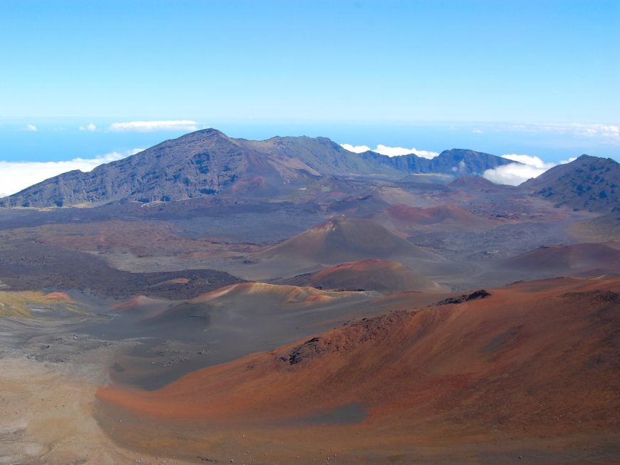 Volcanic crater with rock formations and sand in various shades of red, green, and brown