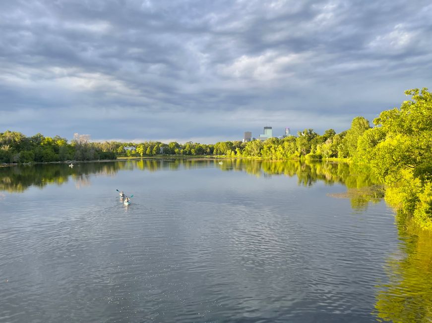 Lake surrounded by trees with the Minneapolis skyline in the background