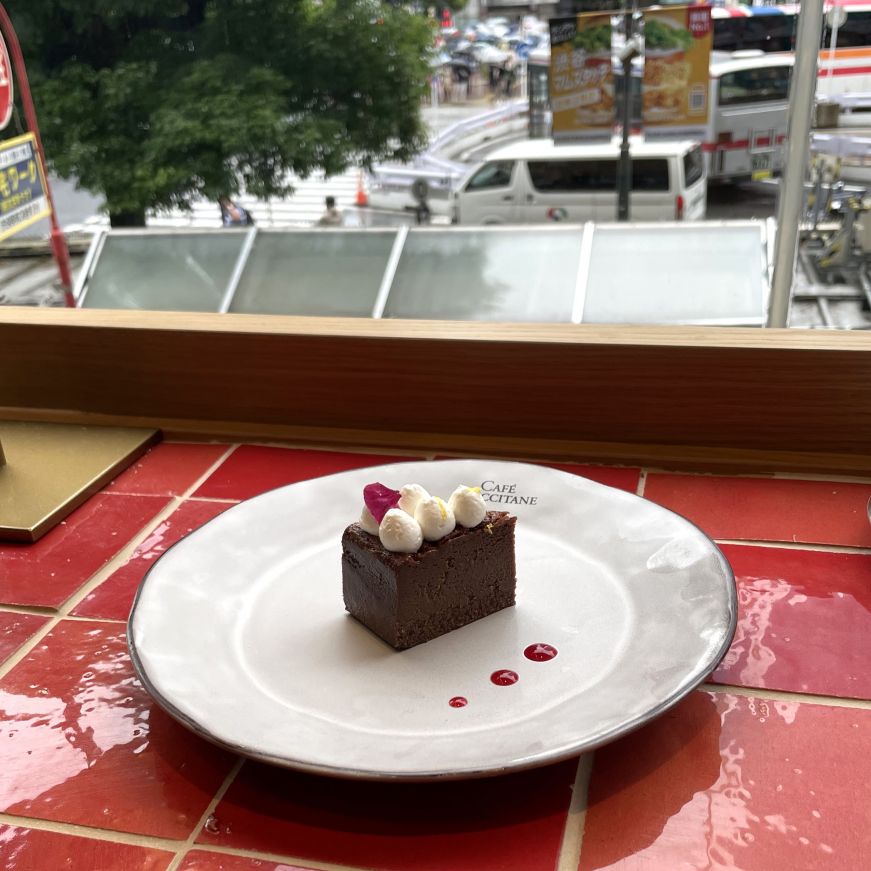 Small chocolate cake with a busy street scene through the window in the background