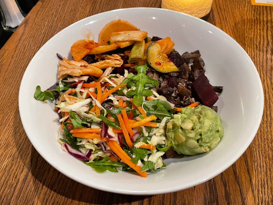 Bowl of whole grains topped with beets, kimchi, mushrooms, slaw, and a scoop of guacamole