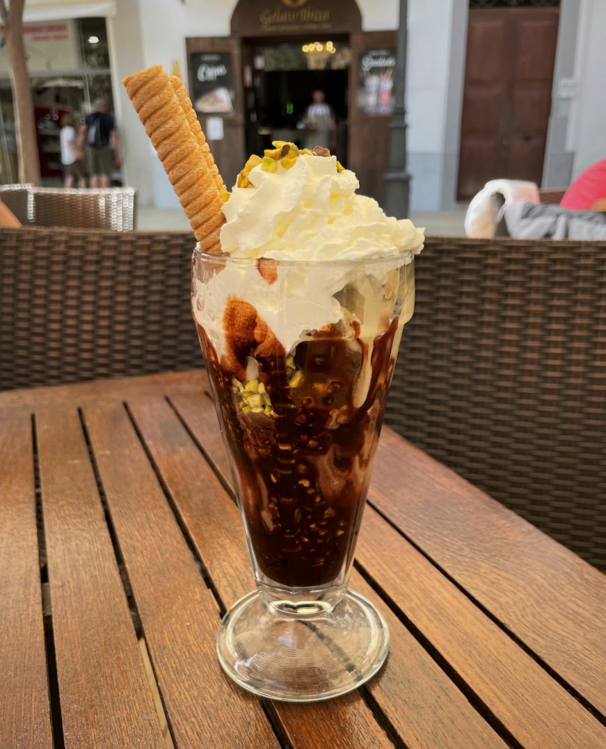 Sundae in a glass dish with chocolate sauce, whipped cream, and chopped pistachios