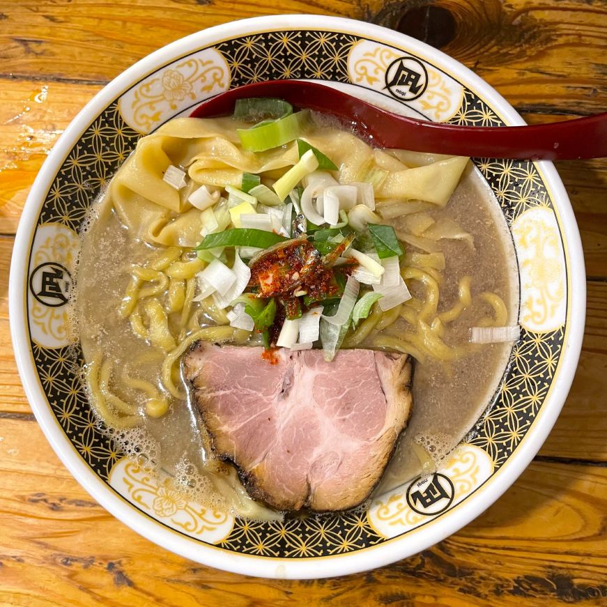 Bowl of ramen topped with a piece of pork, green onions, and chili paste