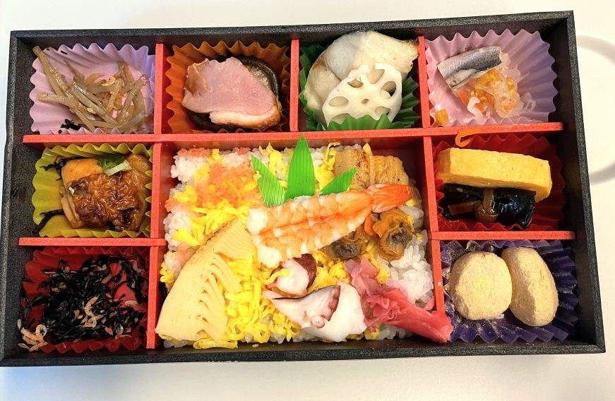 Bento box divided into several small boxes filled with rice, fish, pickles, meat, and other items