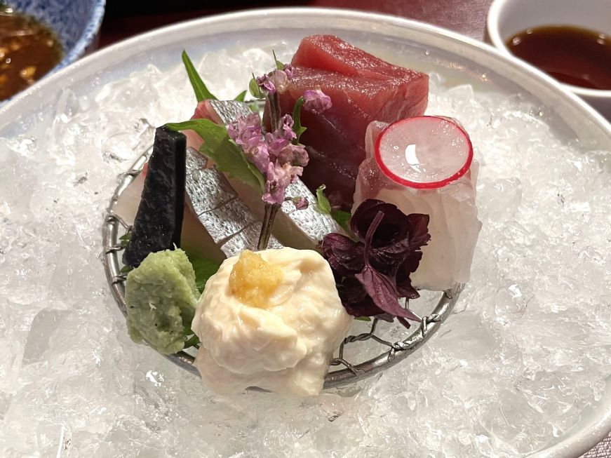 Pieces of raw fish on a small plate surrounded by crushed ice