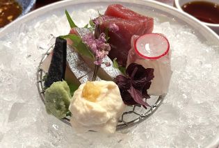 Small plate of sashimi garnished with flowers and resting on a bed of ice